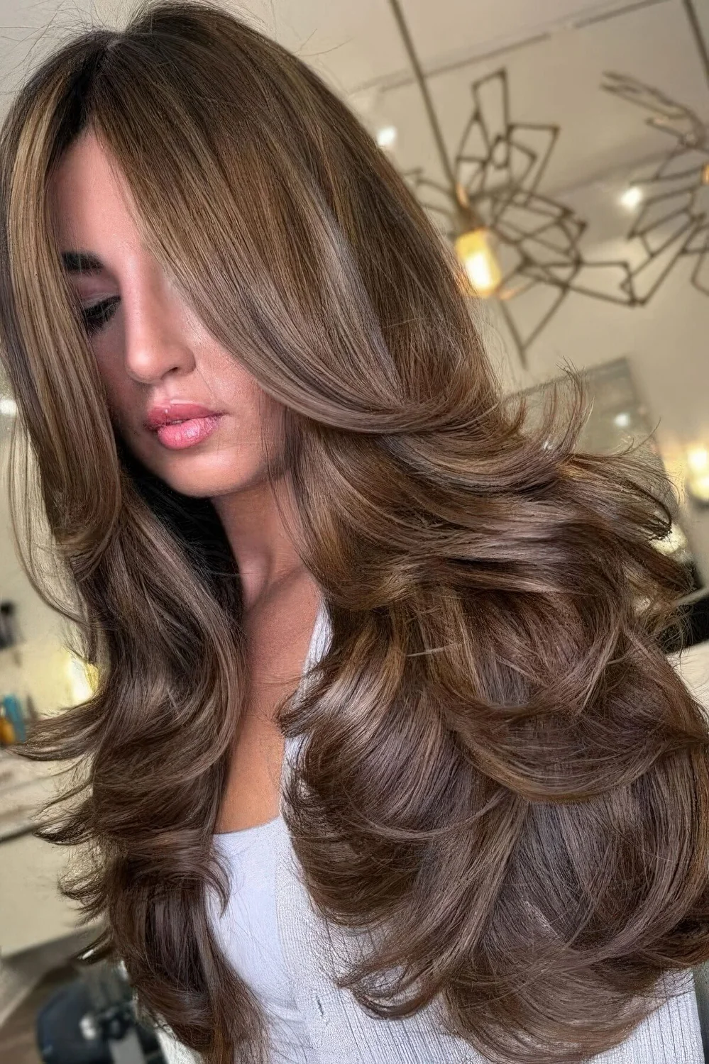 Long brunette butterfly haircut with curtain bangs and a bit of golden blonde balayage.