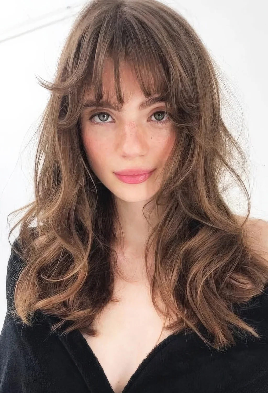 Long brunette butterfly haircut with messy waves and wispy bangs.
