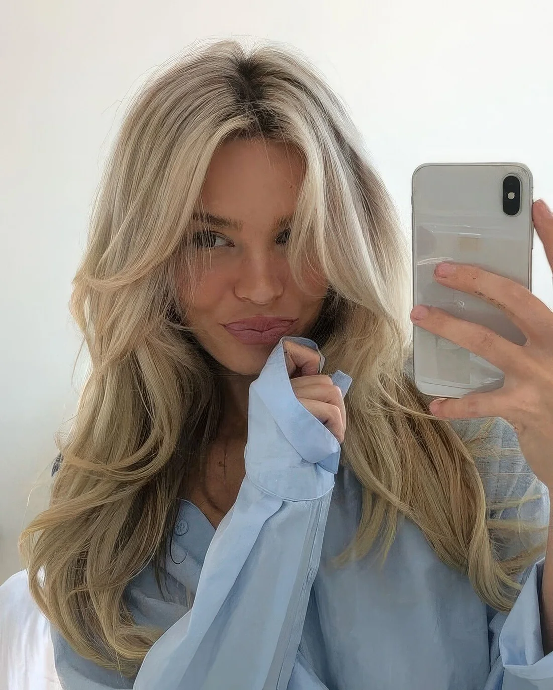 Bleached blonde butterfly haircut on long hair, with a darker root, wavy ends and a bit of volume.