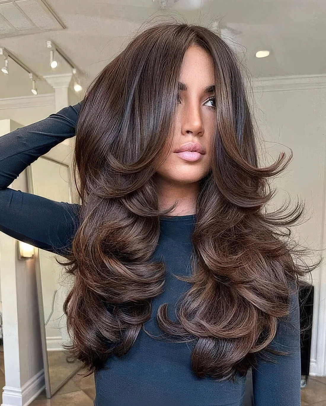 Dark brown butterfly haircut on long hair, with a lot of volume and curtain bangs.