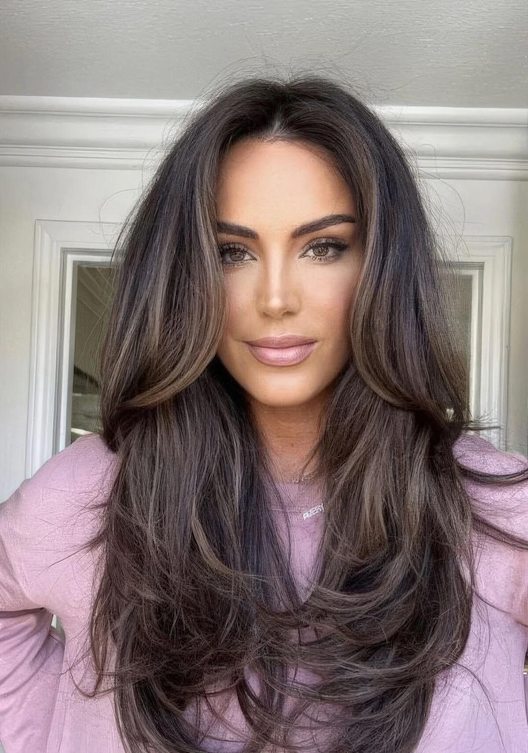 Dark brown butterfly haircut with caramel highlights and long curtain bangs, curled ends and dimension.