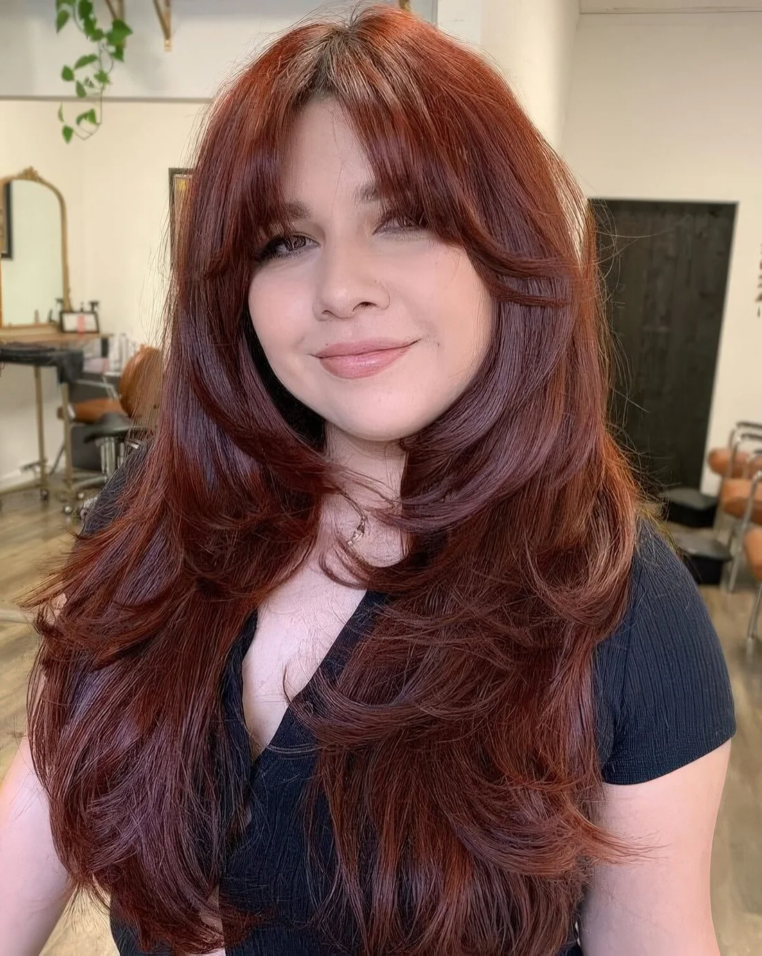 Auburn long butterfly haircut with curtain bangs, curled ends and a lot of volume.