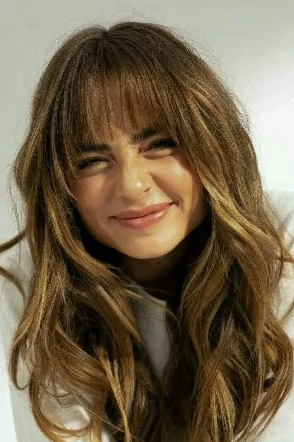 Long bronde butterfly haircut with side and wispy bangs and textured waves.
