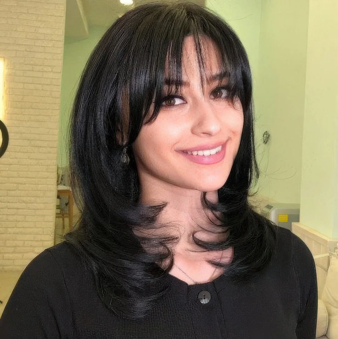 Black medium butterfly haircut with wispy to curtain bangs and curled ends.