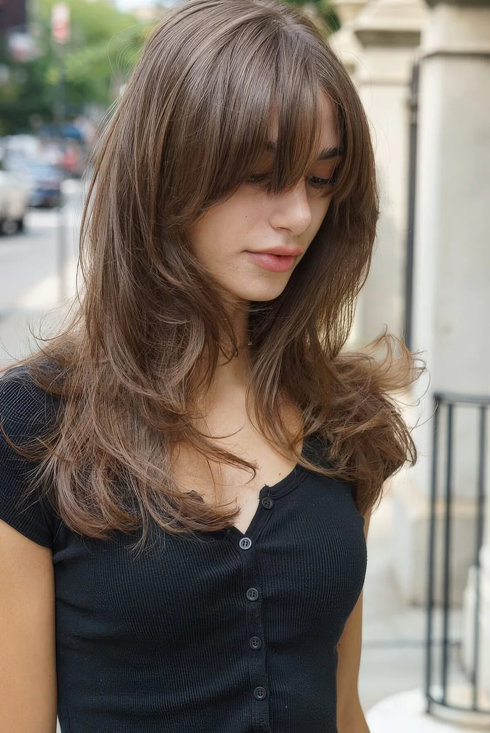 Chic light brunette long butterfly haircut with wispy bangs and waves.