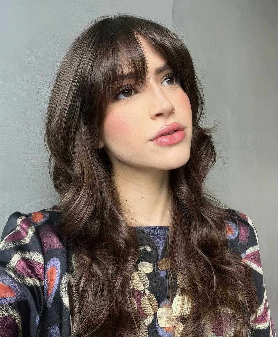 Dark brunette long butterfly haircut with wispy to bottleneck bangs and waves.
