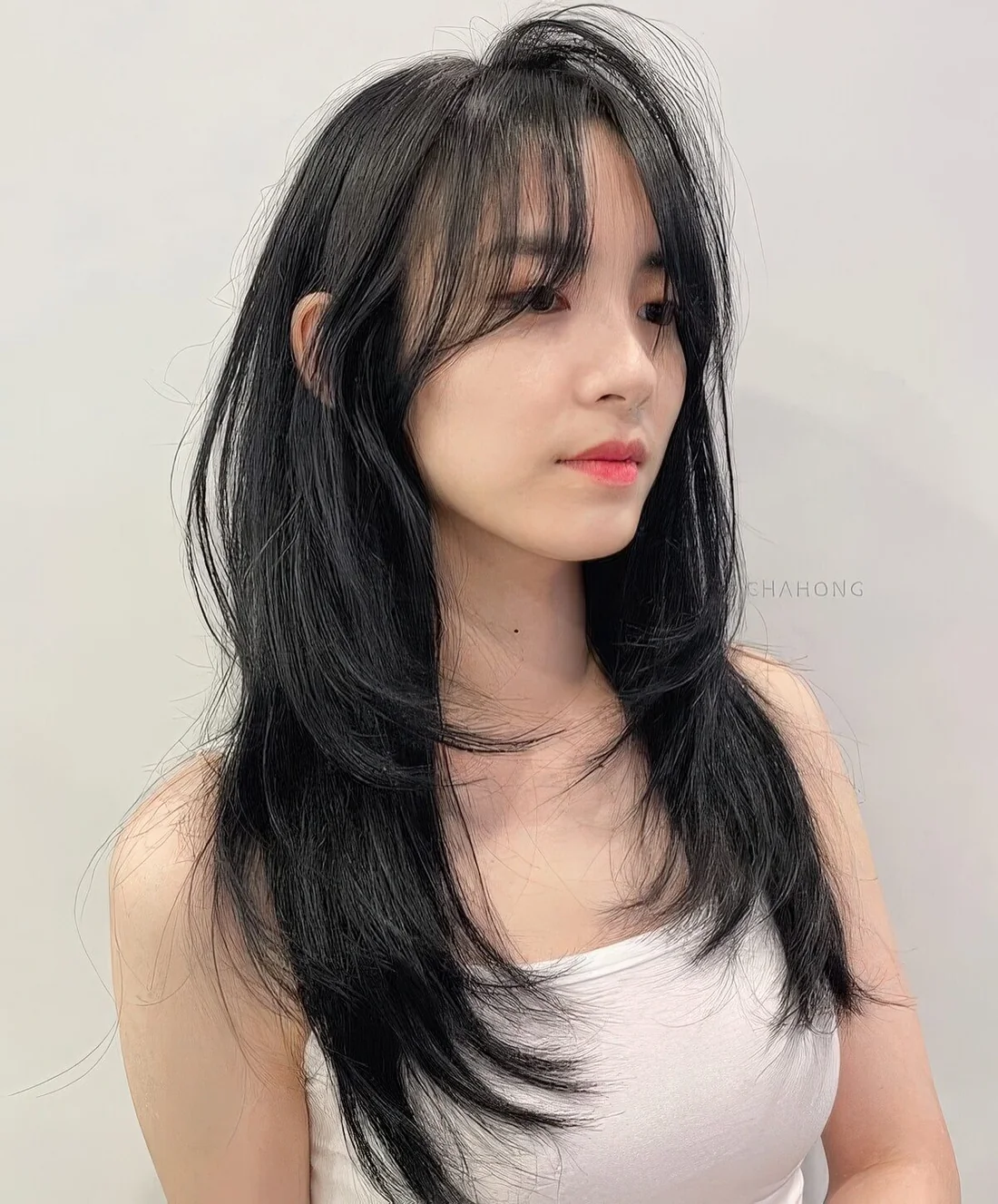 Long black butterfly haircut with face-framing layers and wispy bangs plus curled ends.