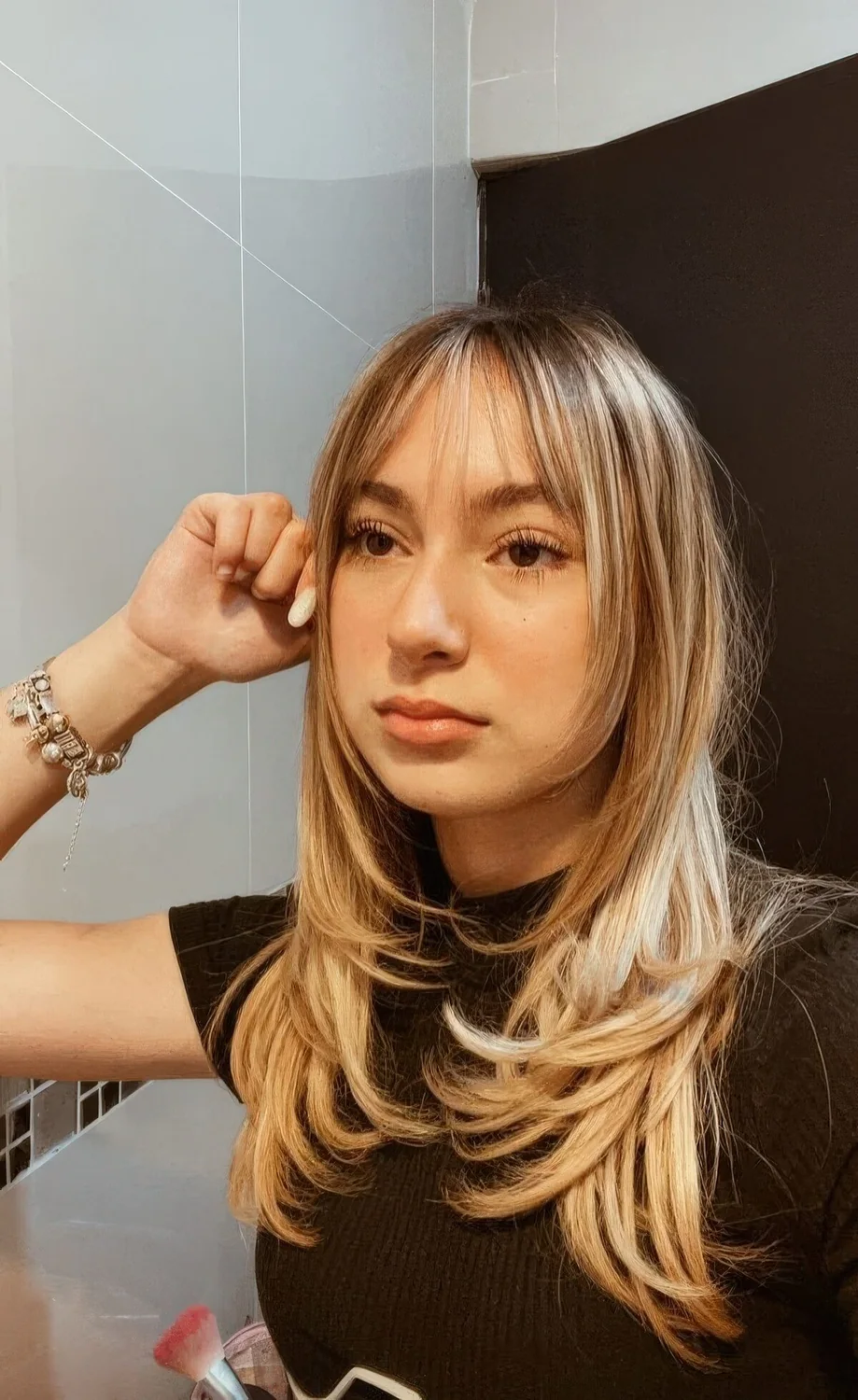 Long blonde butterfly hairstyle with wispy bangs and face-framing layers plus curled ends.