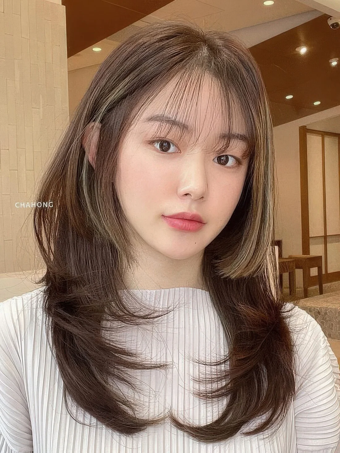 Long brunette butterfly haircut with golden blonde balayage and wispy bangs plus curled ends.