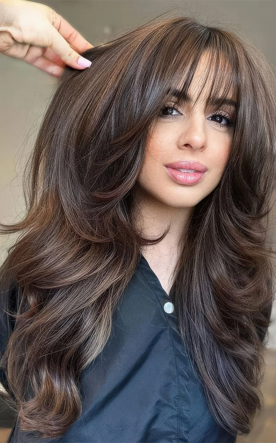Long dark brunette butterfly hairstyle with a bit of balayage, dimension and wispy bangs.