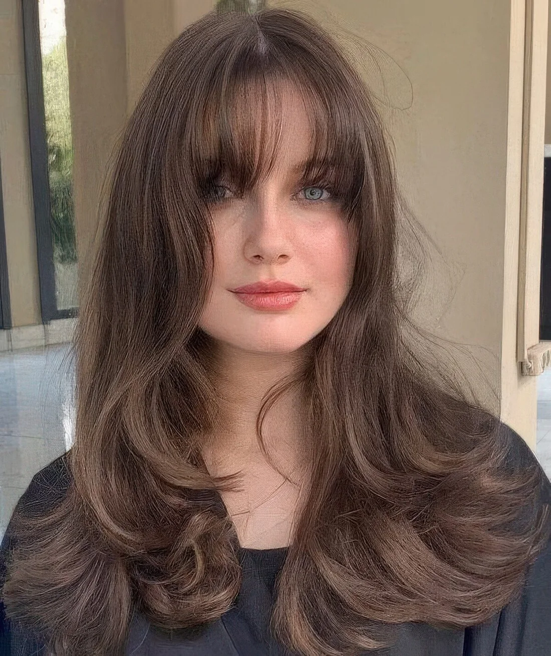 Brunette butterfly haircut with waves and wispy bangs.