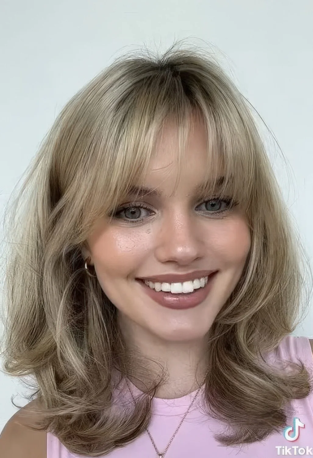Medium blonde butterfly haircut with wispy bangs and waves.