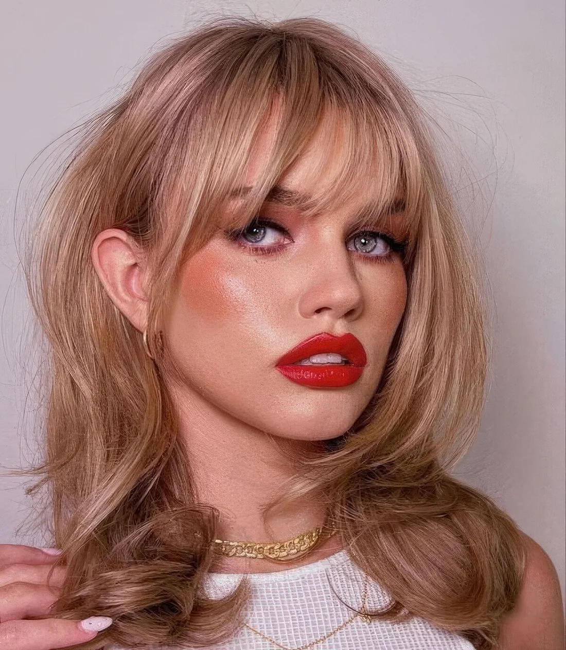 Medium-length butterfly haircut with wispy bangs and curled ends plus dimension and a lovely soft blonde shade.