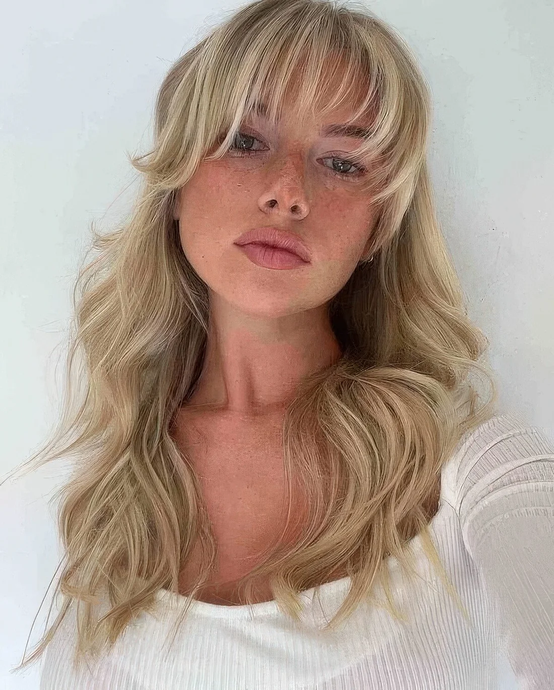 Long blonde hair with layers and waves plus wispy and curtain bangs paired to frame the face in the most beautiful way.