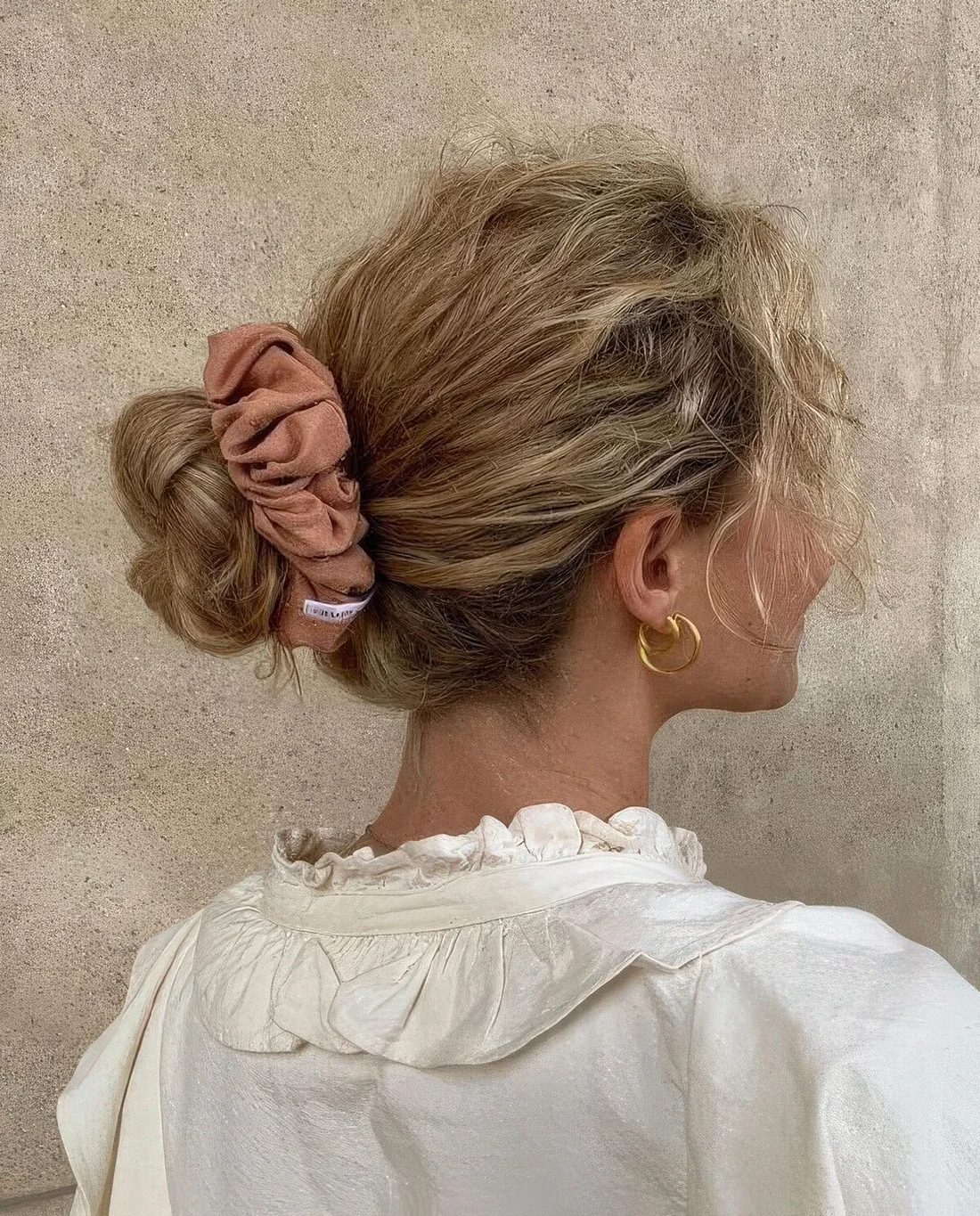 Classic ballerina bun done on curly hair, with face-framing bangs and accented with a pink scrunchie.