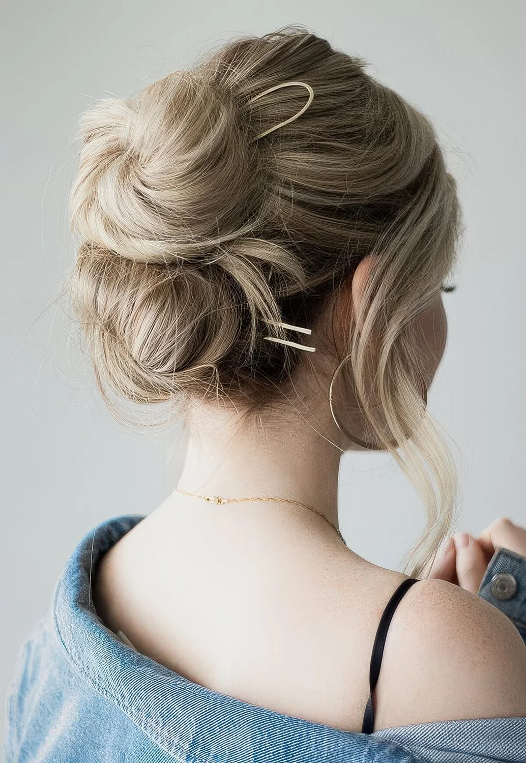 Double bun, a midi and low one, with a volumetric top and face-framing hair plus bold modern hair pins for long hair.