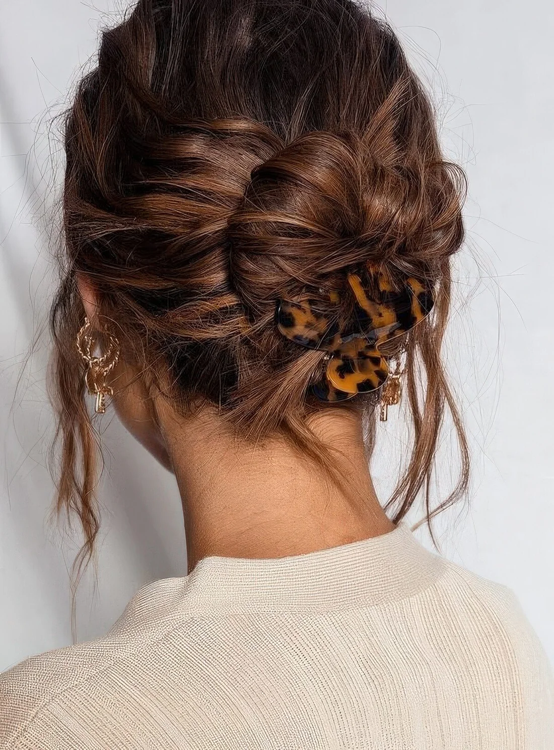 Low ballerina bun on curly hair, with a curly top and face-framing hair, a leopard print hair clip to secure the bun.