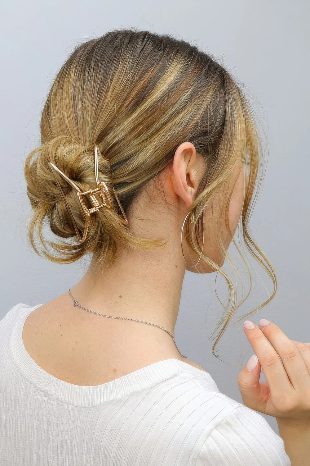 Low ballerina bun with a sleek top, face-framing hair and a gold hair clip to secure the bun.