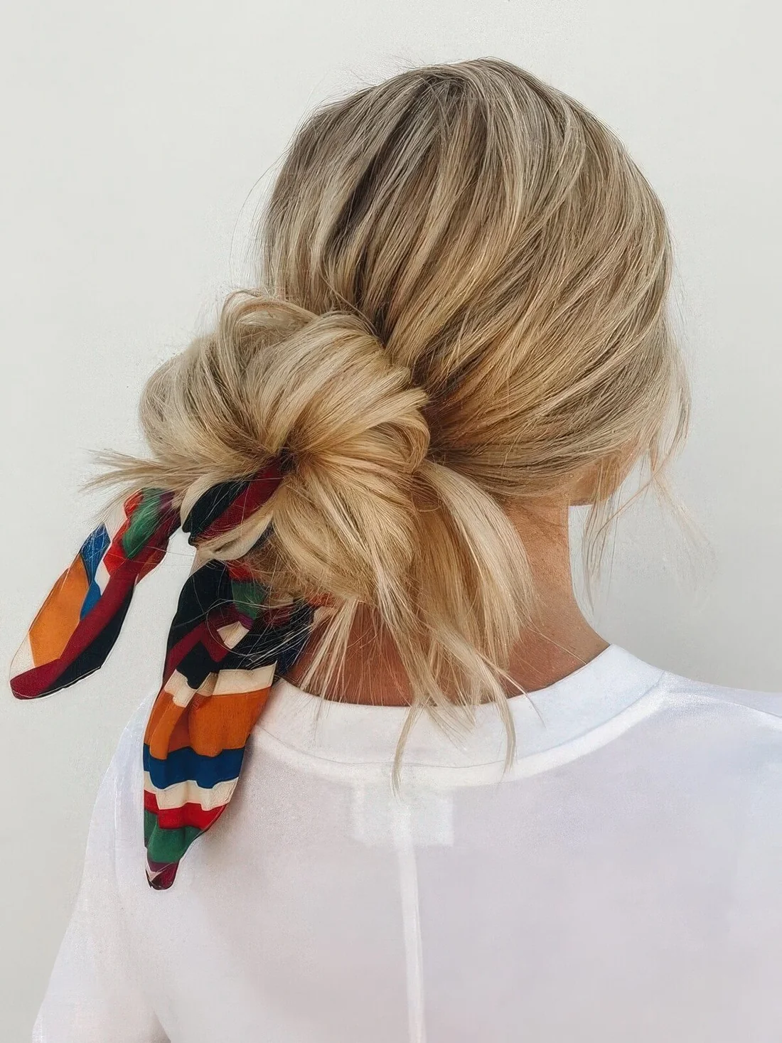 Low ballerina bun with a textural top and a colorful head scarf to secure the hair and keep it in place.