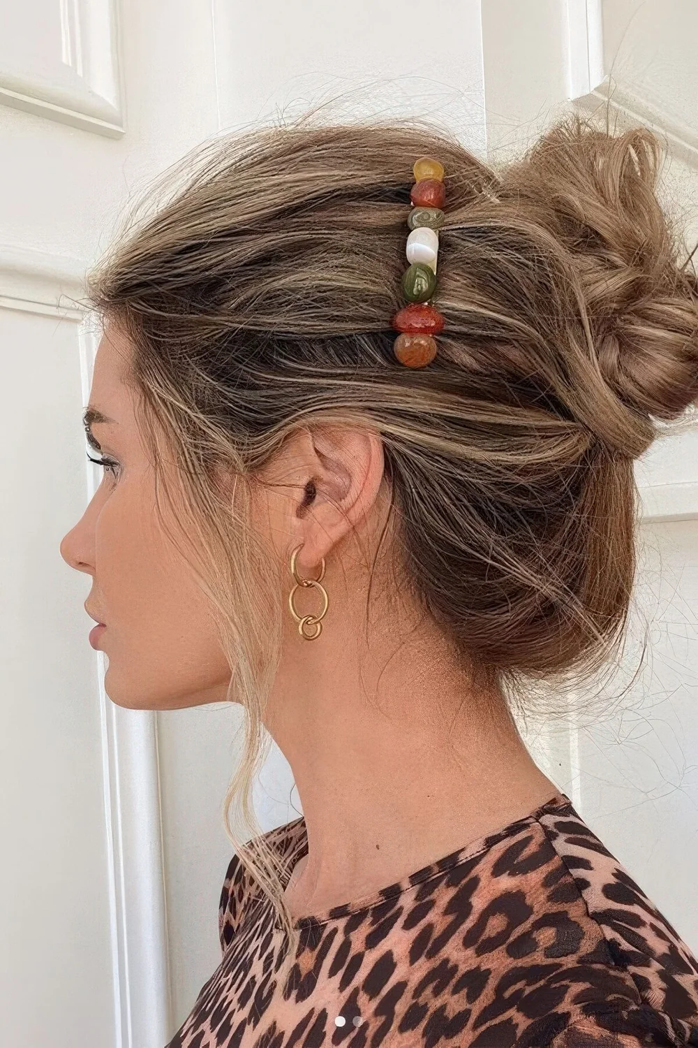 Messy and volumetric midi bun with some hair down and a gemstone hair clip.