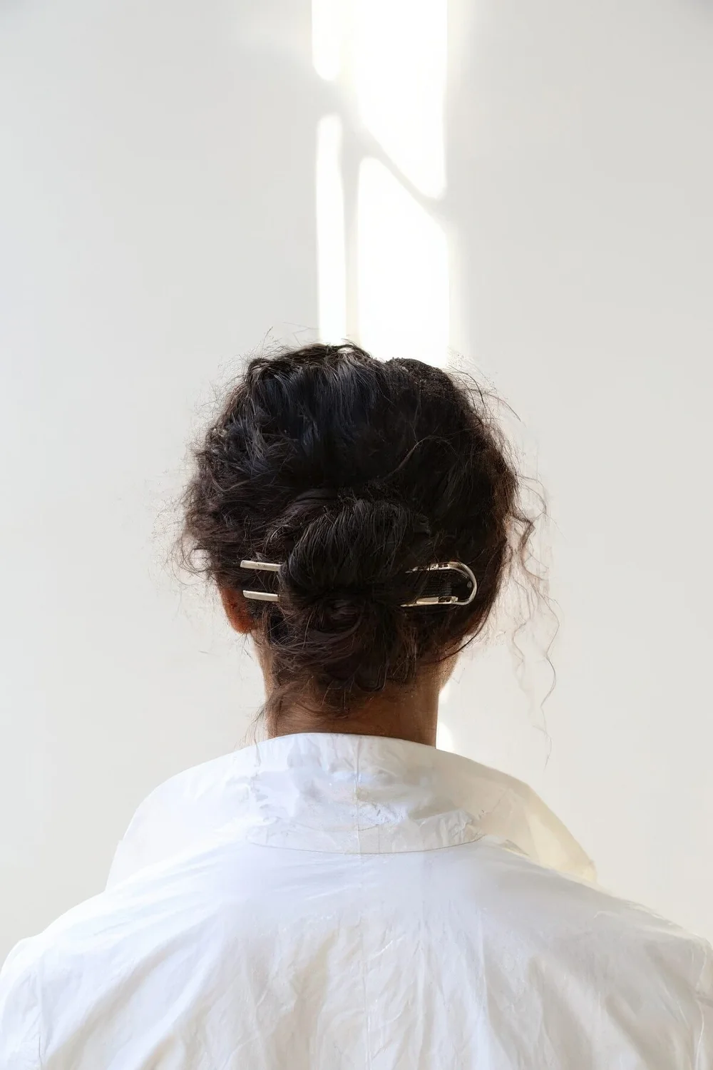 Messy curly midi bun with a volumetric curly top and a shiny hair pin are a cool and fresh modern combo.