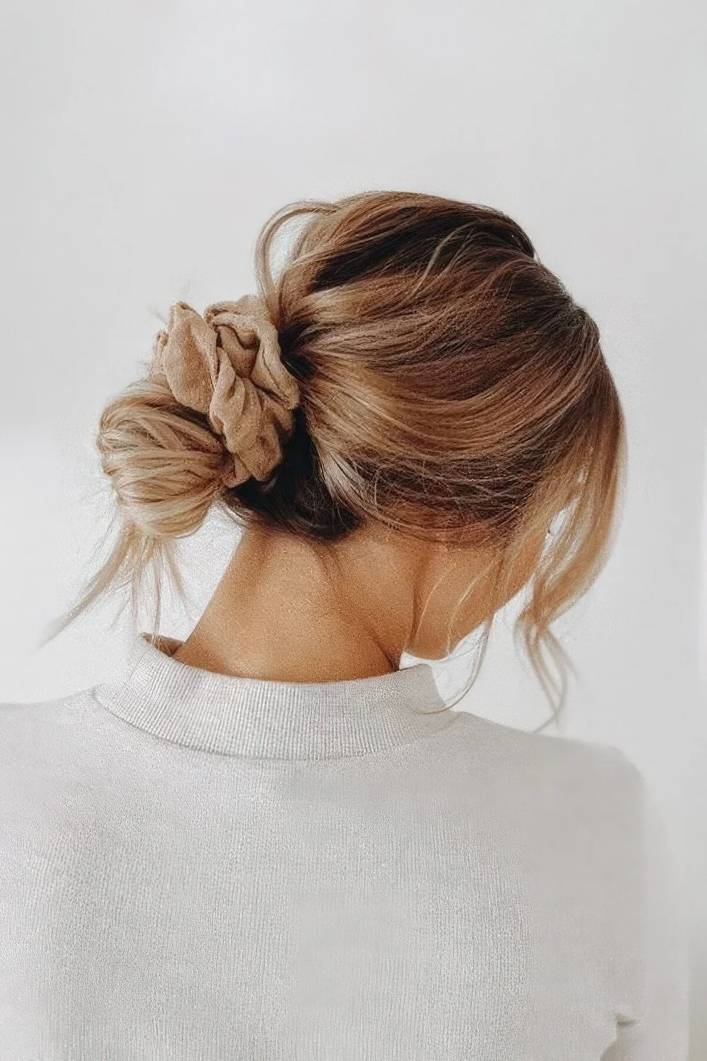 Messy low bun with a volume on top, face-framing bangs and a blush scrunchie are a great hair combo.