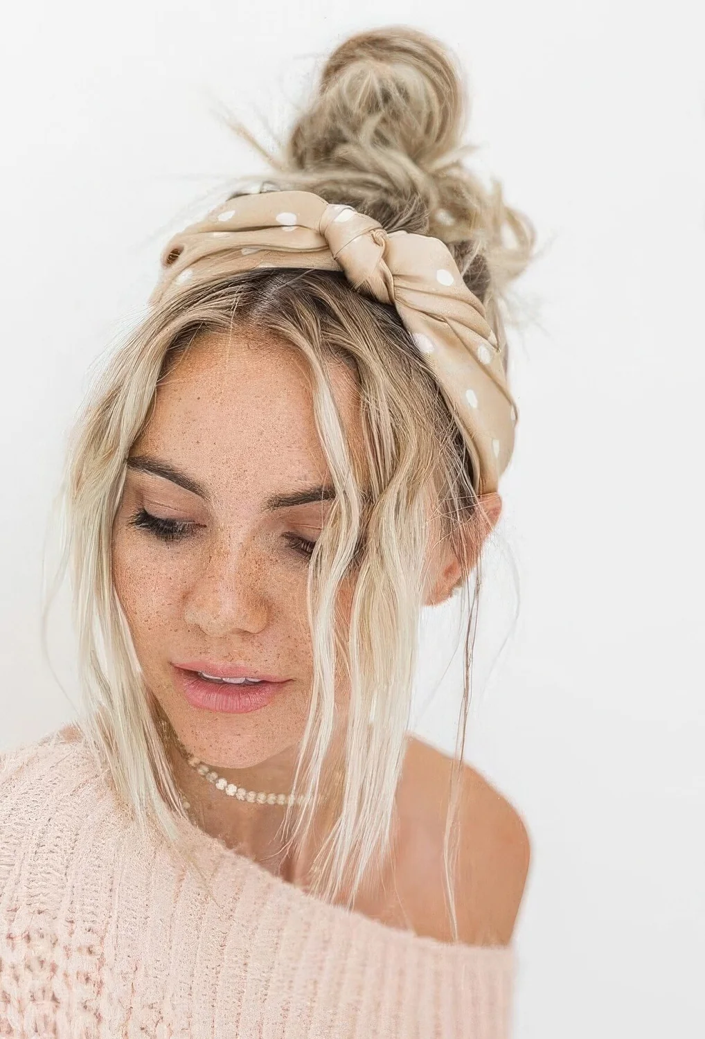 Messy top knot with a messy top, face frmaing bangs and a blush polka dot headband for a slight accent.