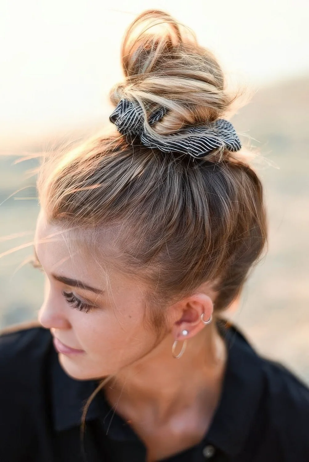 Messy top knot with a sleek top and a striped scrunchie accenting the look.
