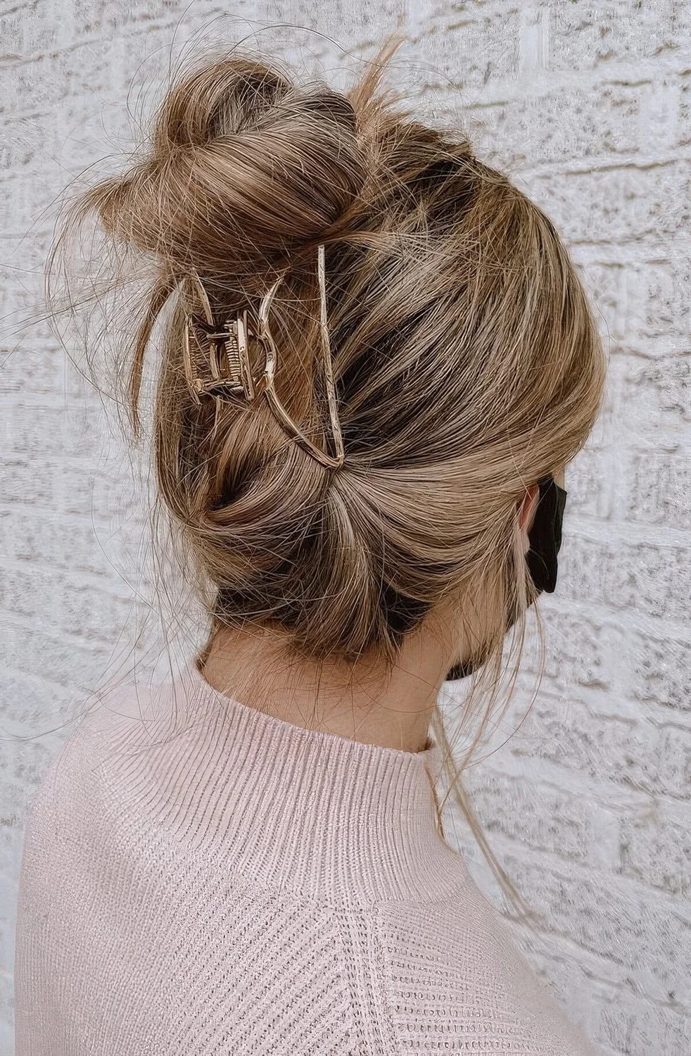 Messy top knot with some hair secured with a gold hair clip and a messy top.
