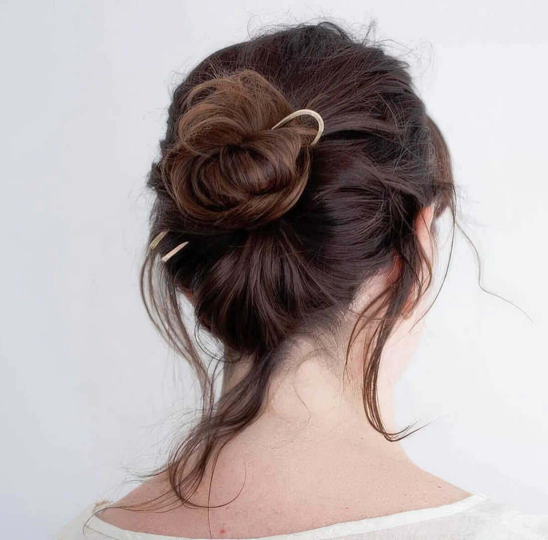 Messy updo with a lot of volume, a midi bun, some hair down and a single hair pin for an accent and to secure the hair.
