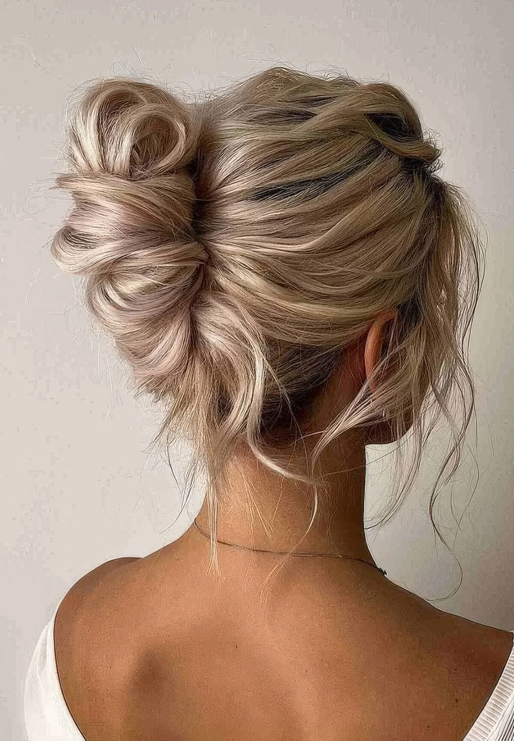 Messy wavy French chignon hairstyle with a messy volumetric top and some face-framing hair.