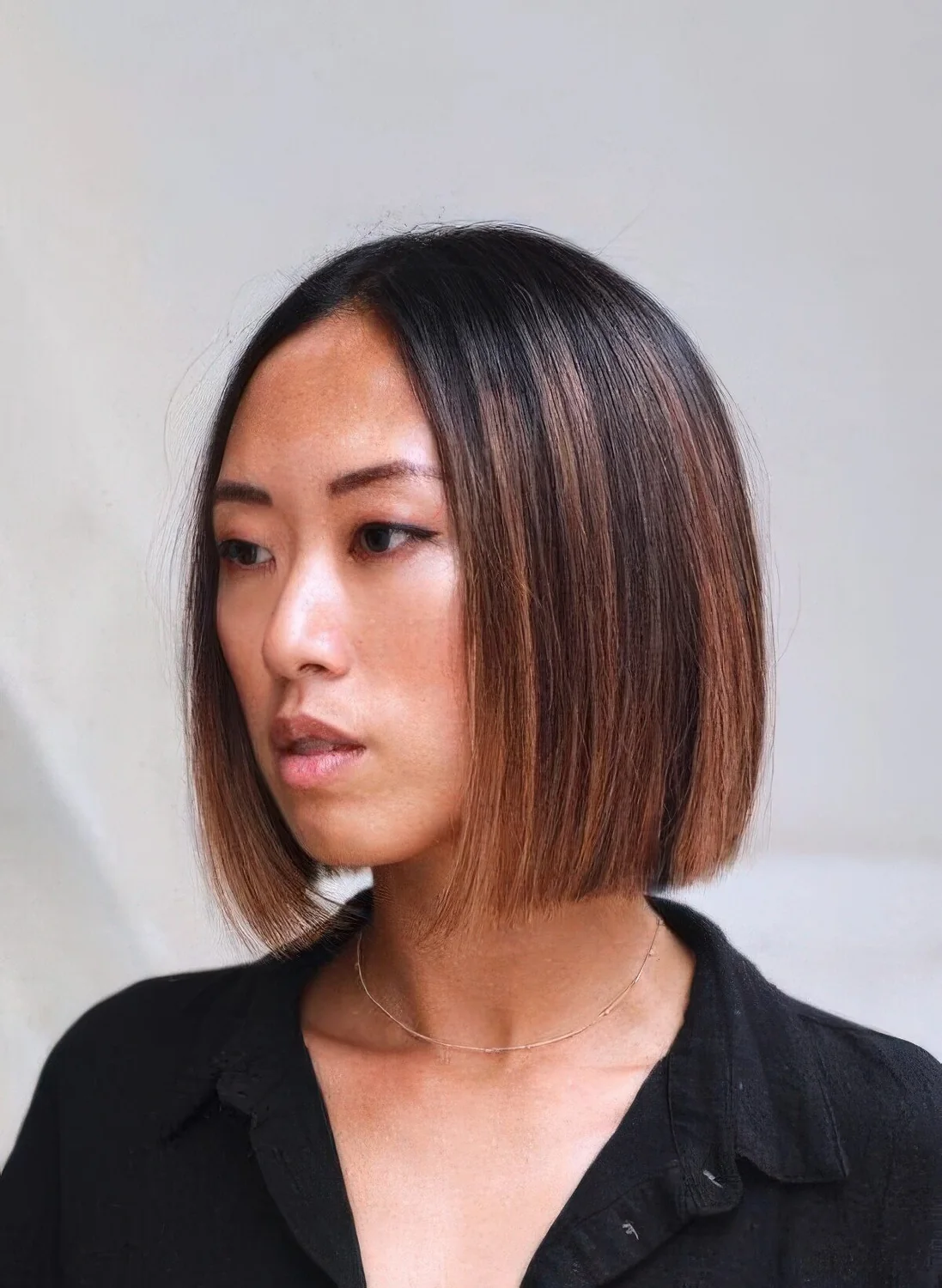 Black chin-length bob with chestnut and copper balayage and a dark root, with straight hair.