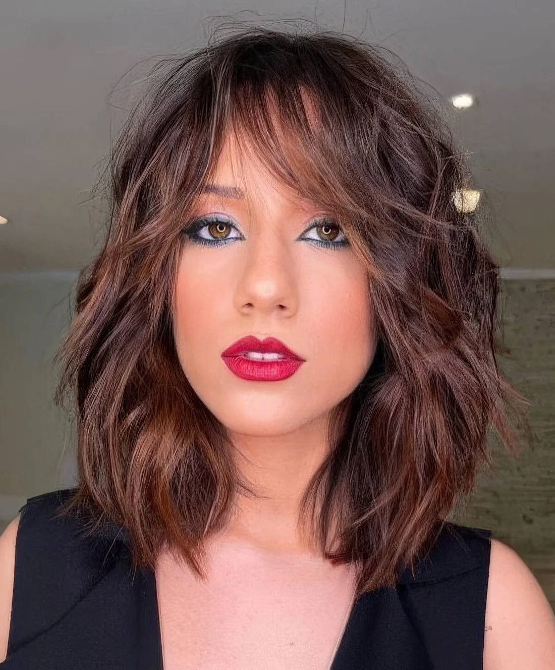Rich brown long bob with caramel balayage and messy waves plus bottleneck bangs.
