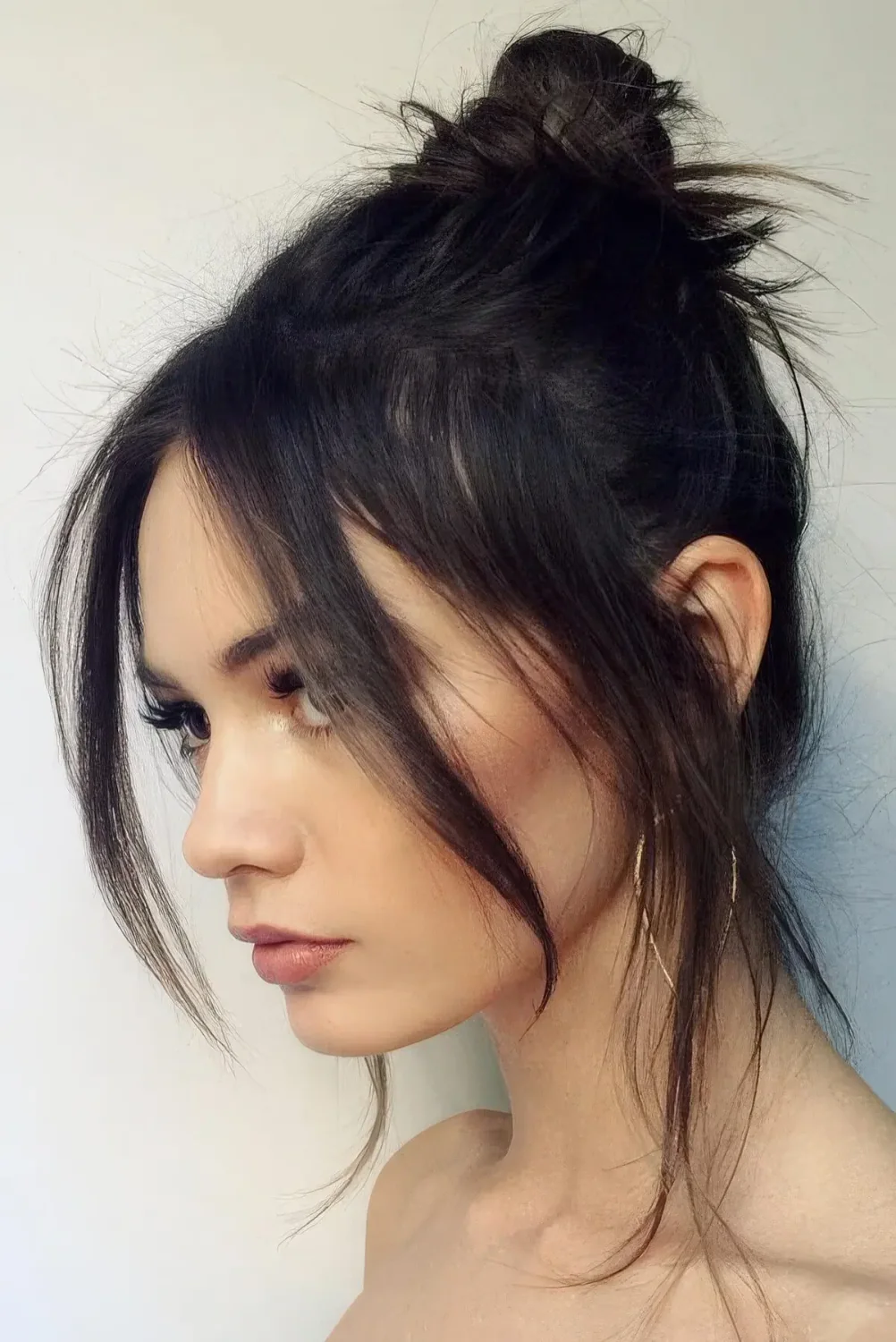 Black messy top knot with chin bangs and some locks down.