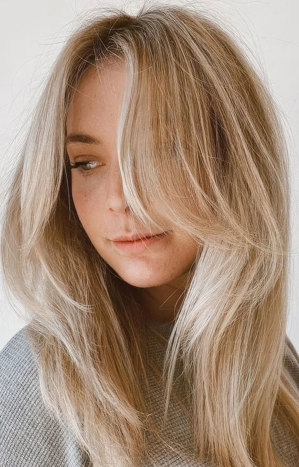 Long blonde hair with icy balayage and chin-length side bangs.