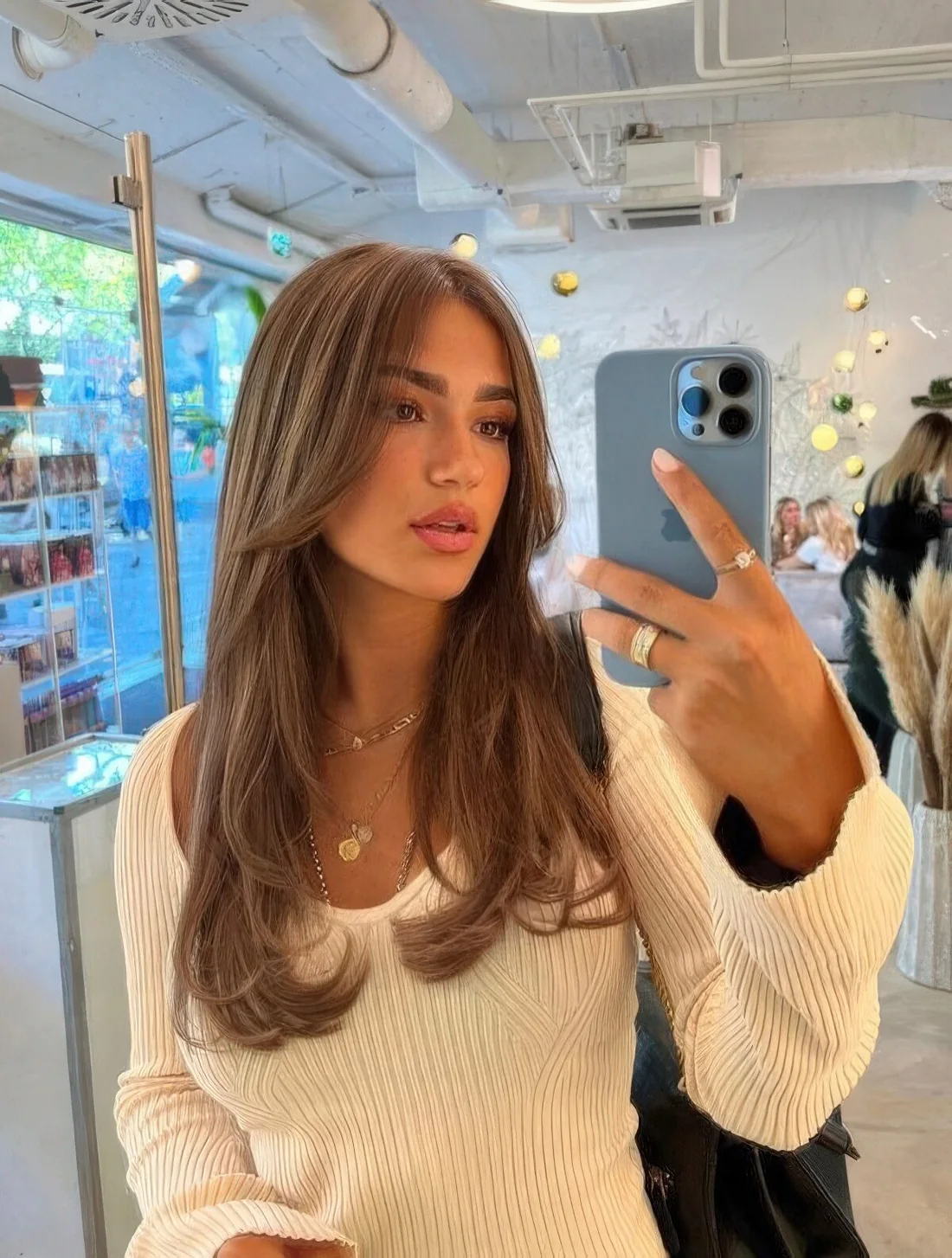 Long brown hair with a cascade effect, a caramel balayage and long curtain bangs.