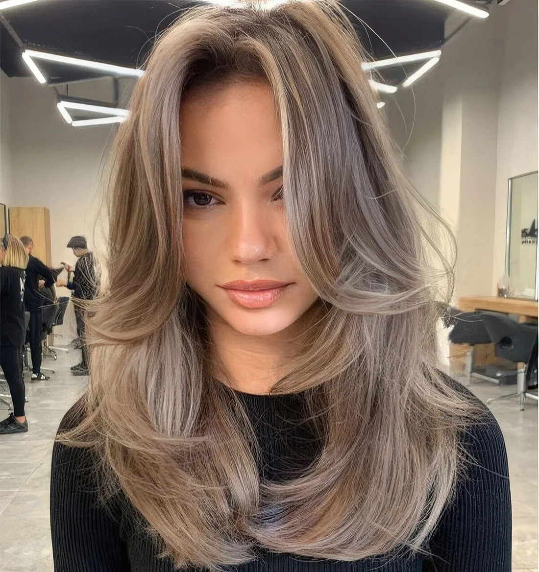 Long mousy brown hair with layers and chin bangs, with lighter accents and a lot of volume.
