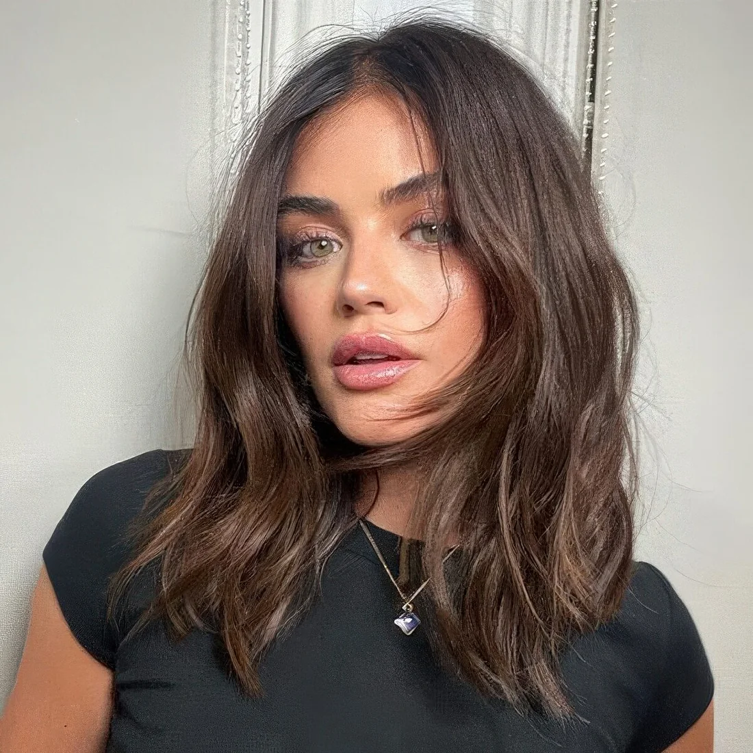 Lucy Hale wearing brunette medium-length hair with some lowlights, chin bangs and waves plus middle part.