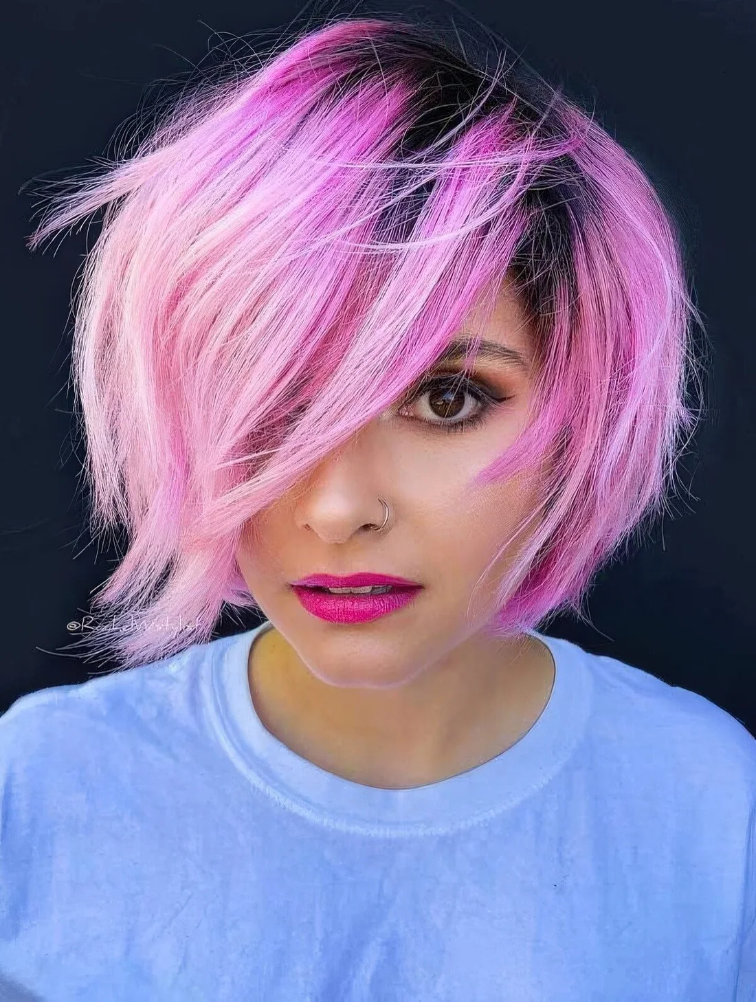 Pink choppy bob with dark roots with sharp layers that.