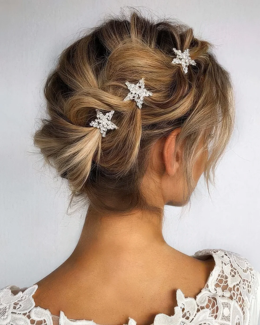 Whimsical updo with a loose braid on one side and star rhinestone hairpins.