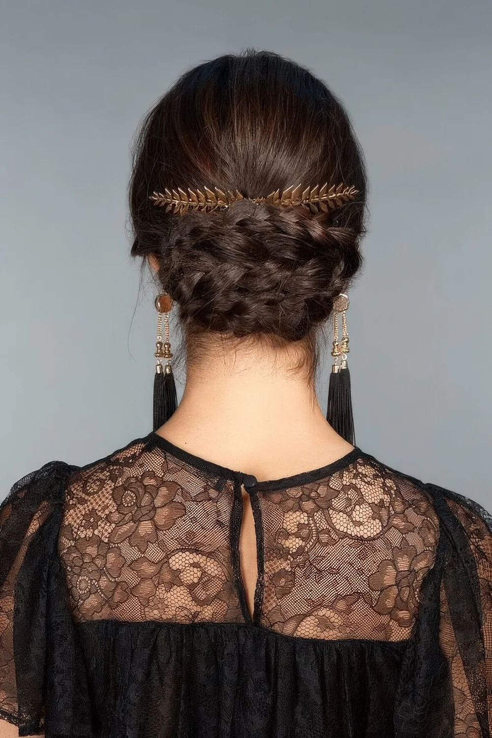 Braided updo with a sleek top, a gold leaf accent and statement earrings for a chic party look.