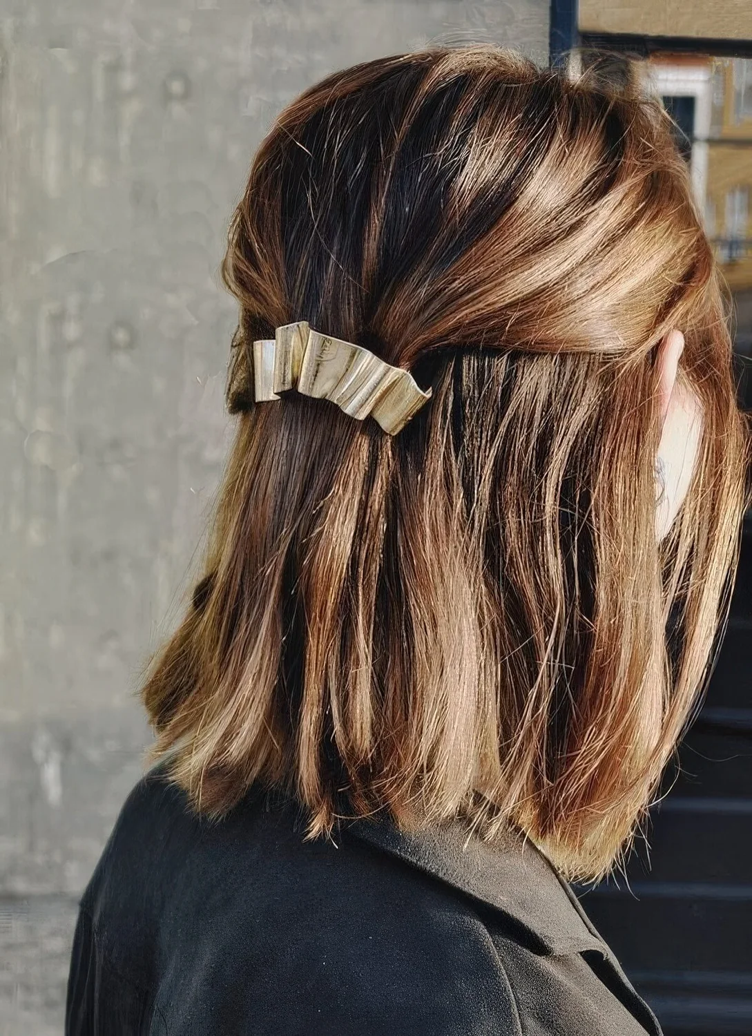 Half updo with a bump on top and straight hair down and a metallic hair barrette for a modern holiday party look.