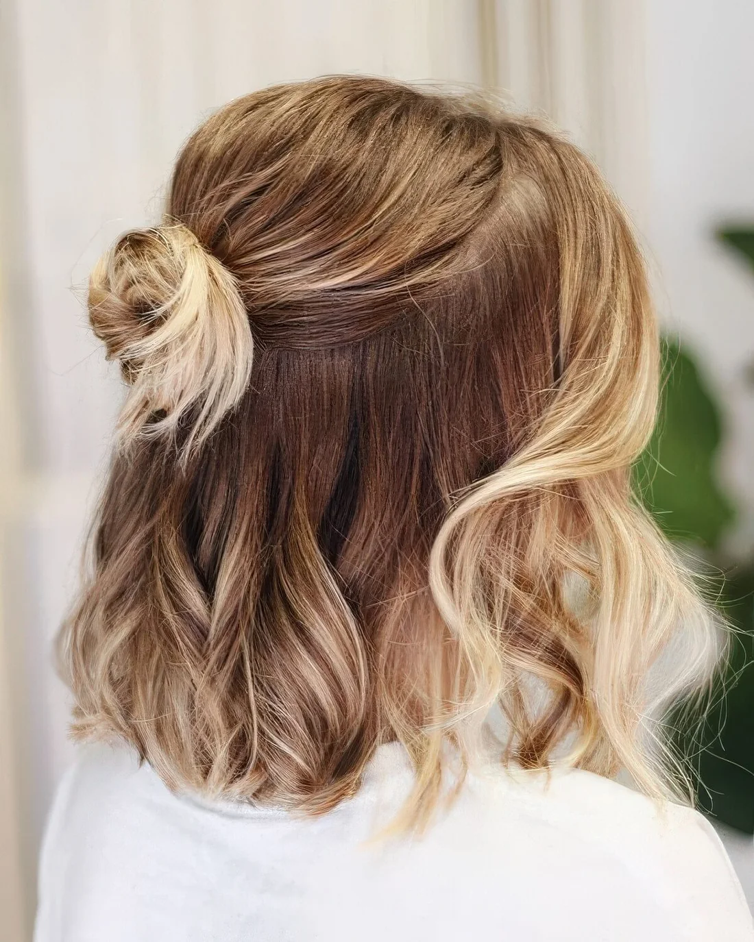 Medium hair half updo with a bump on top, a small bun and waves down plus face-framing hair.