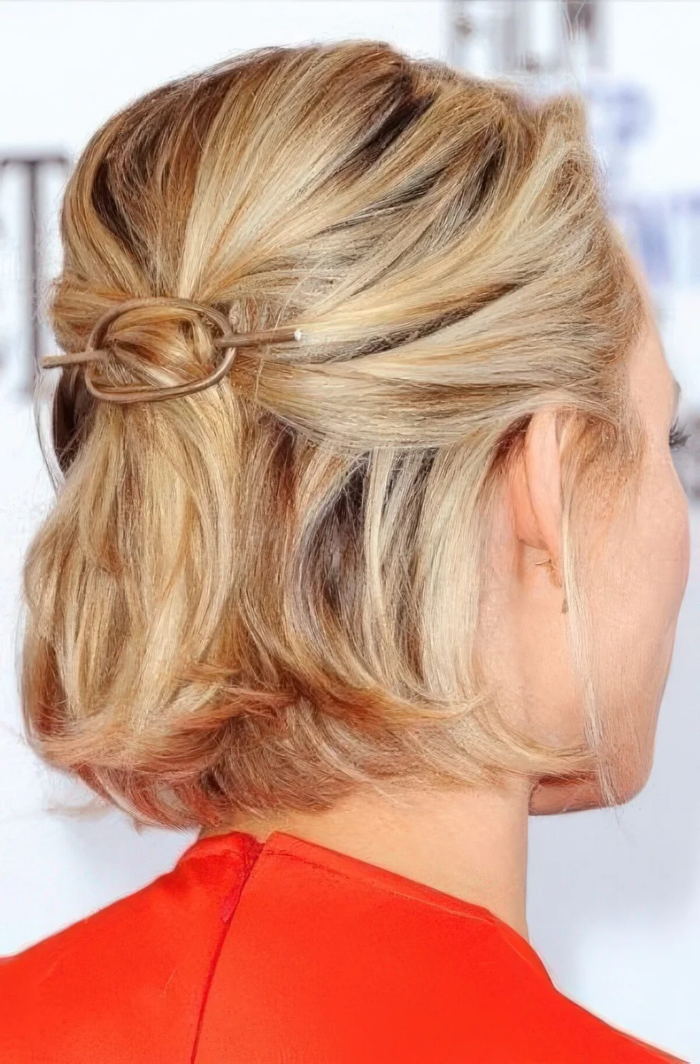 Midi blonde bob styled as a half updo, with a bump on top and a hair piece, with some volume on top.