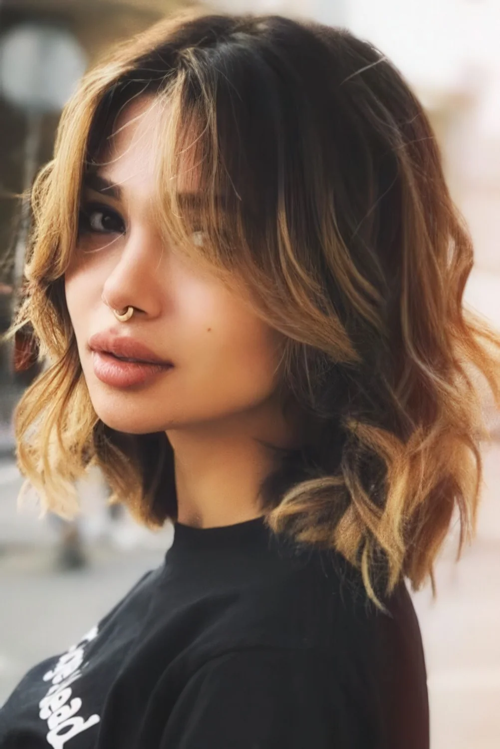 Medium layered haircut with honey blonde balayage and much texture, with curtain bangs.