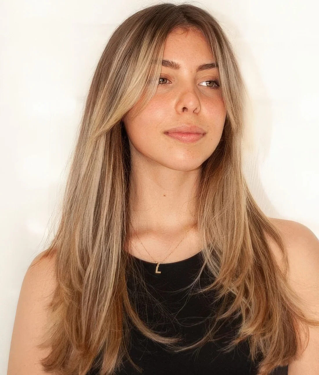 Long hair with warm blonde balayage and with curtain bangs, with much texture.