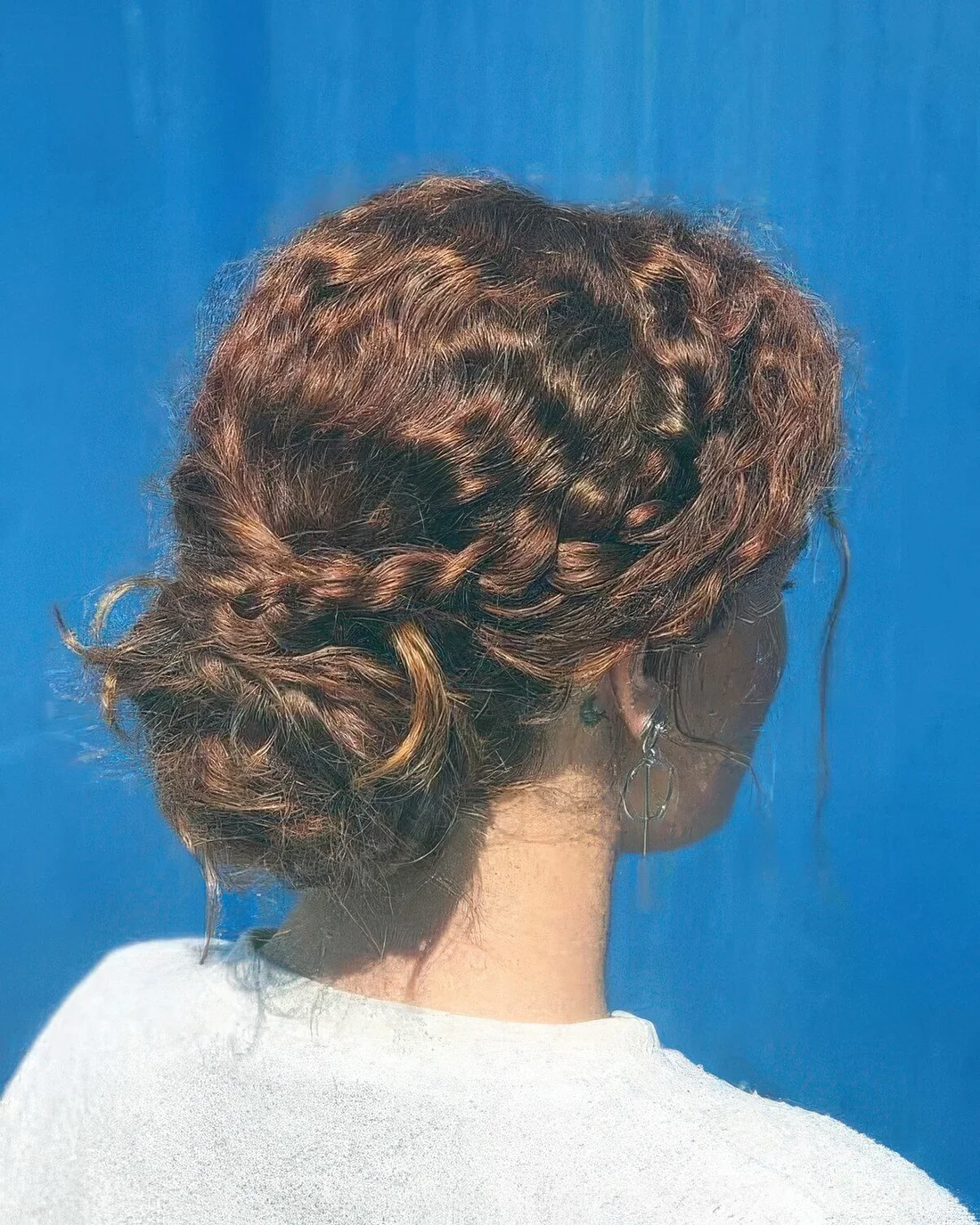 Messy wavy updo with a braided halo and a volumetric low bun plus a curly bump.