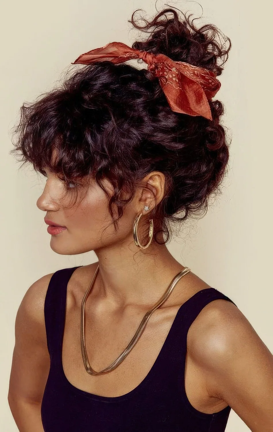 Curly updo on medium hair accented with an orange hair scarf and face-framing bangs to accent the eyes.