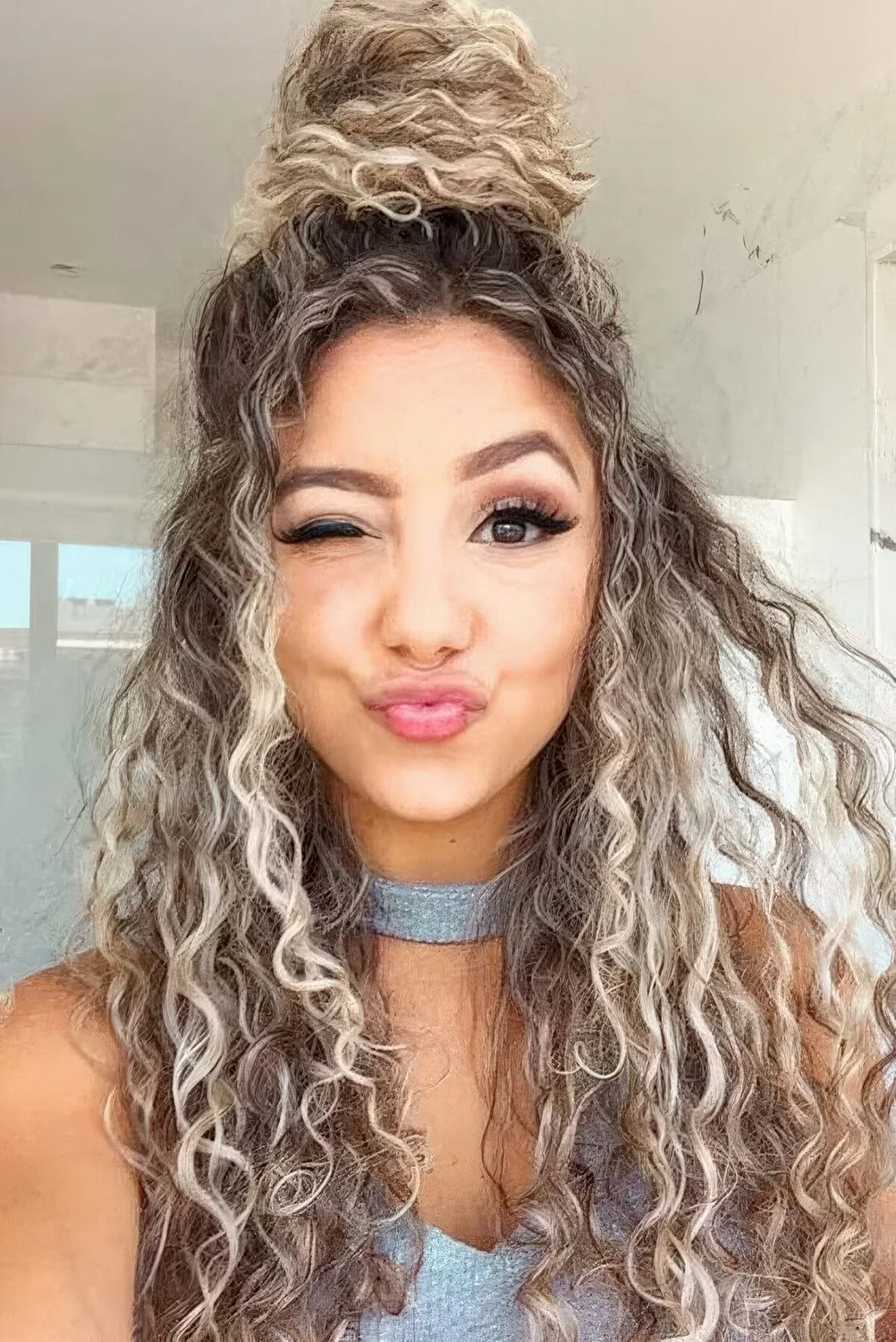 Messy curly half updo with a top knot and curls down.