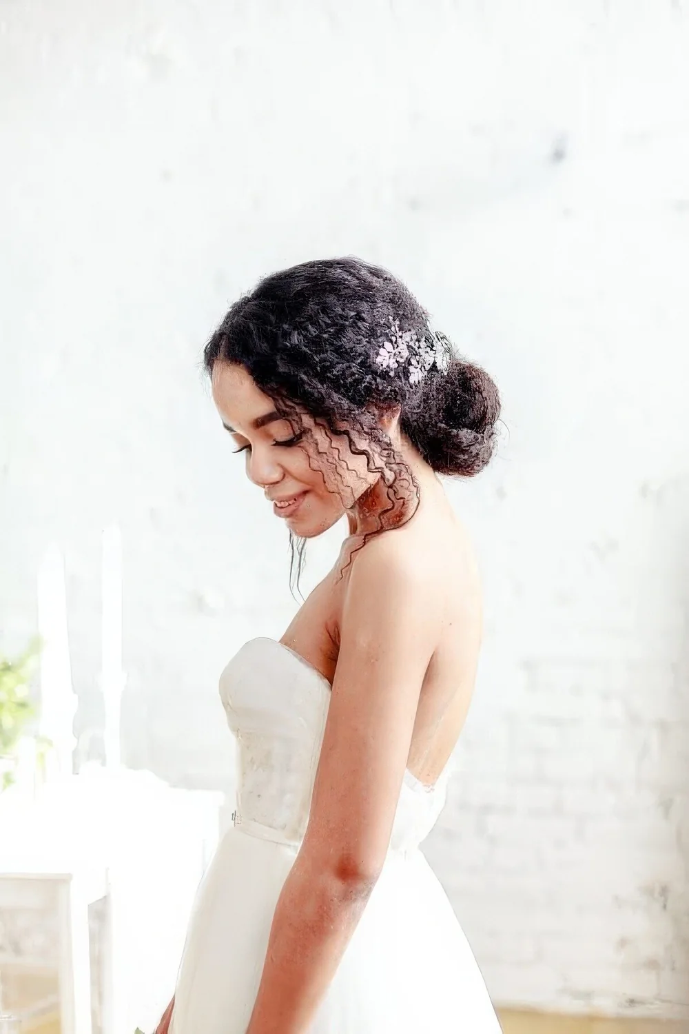 Curly low bun with curls accenting the face and a lovely floral hairpiece.